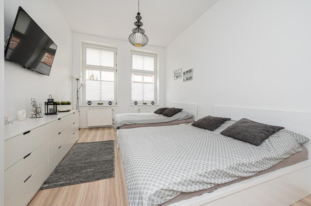 a white bedroom with two beds and a flat screen tv at Mieszkanie przy deptaku Sopot in Sopot