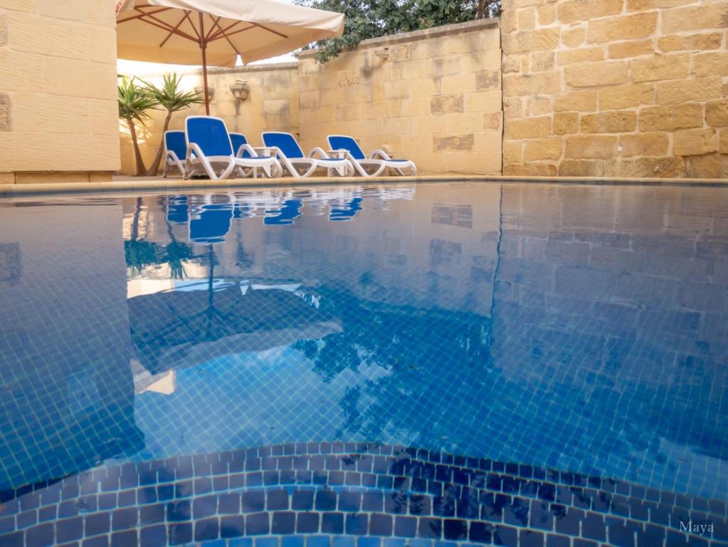 a swimming pool with blue chairs and an umbrella at Sunny Villa in Nadur