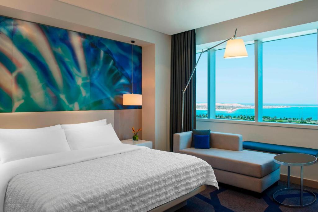 a bedroom with a bed and a chair and a large window at Le Royal Meridien Abu Dhabi in Abu Dhabi