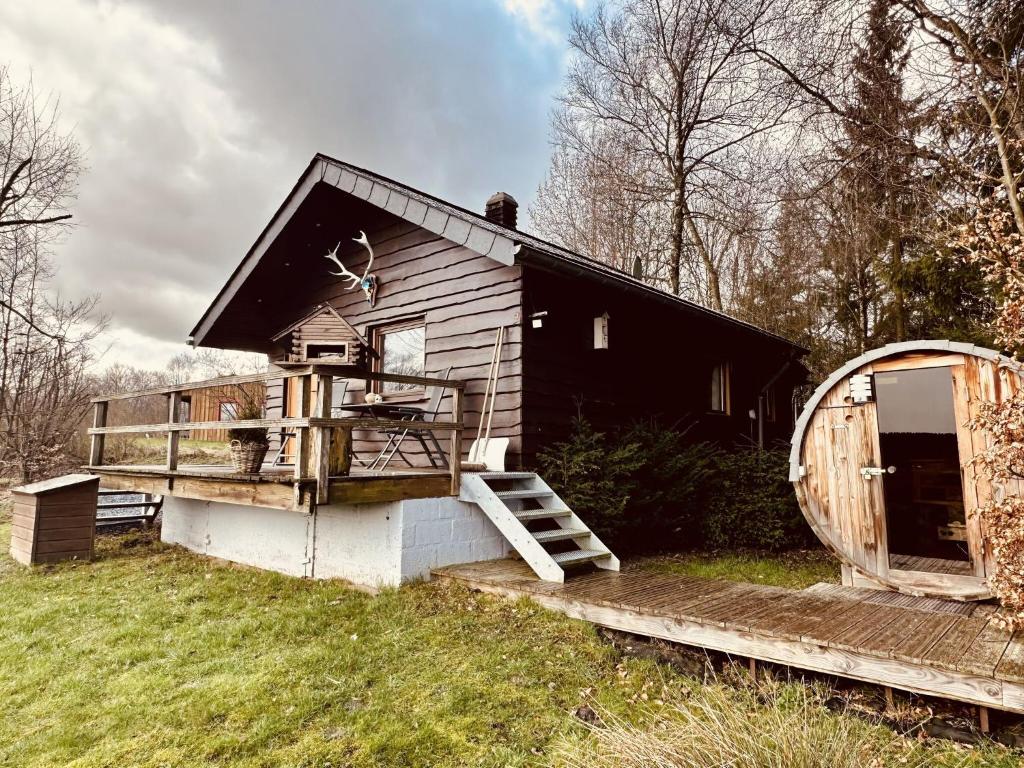 een klein huis met een veranda en een wiel bij Rustic Chalet ultimate relaxation in the forest in Sourbrodt