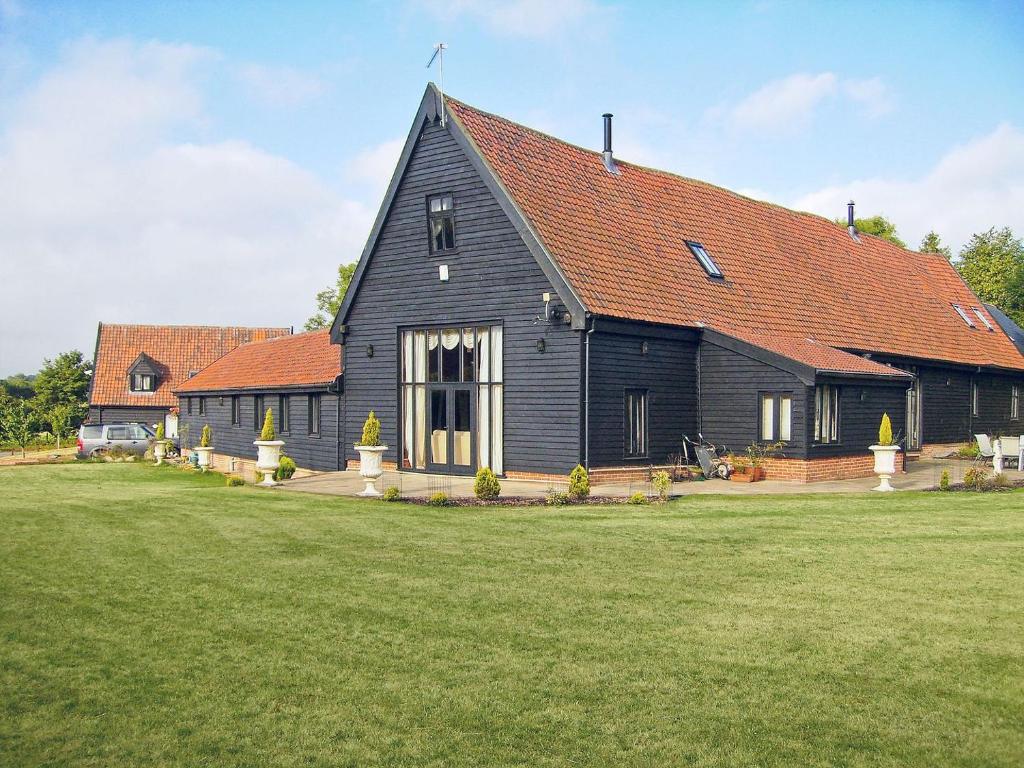 a black barn with a red roof on a field at Doves Barn in Needham Market