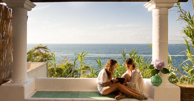 Due donne sedute su un portico con vista sull'oceano di La rosa dei venti a Procida