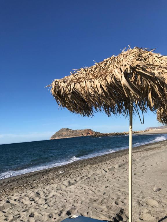 a straw umbrella on a beach with the ocean at Kydonia apartments in Plataniás