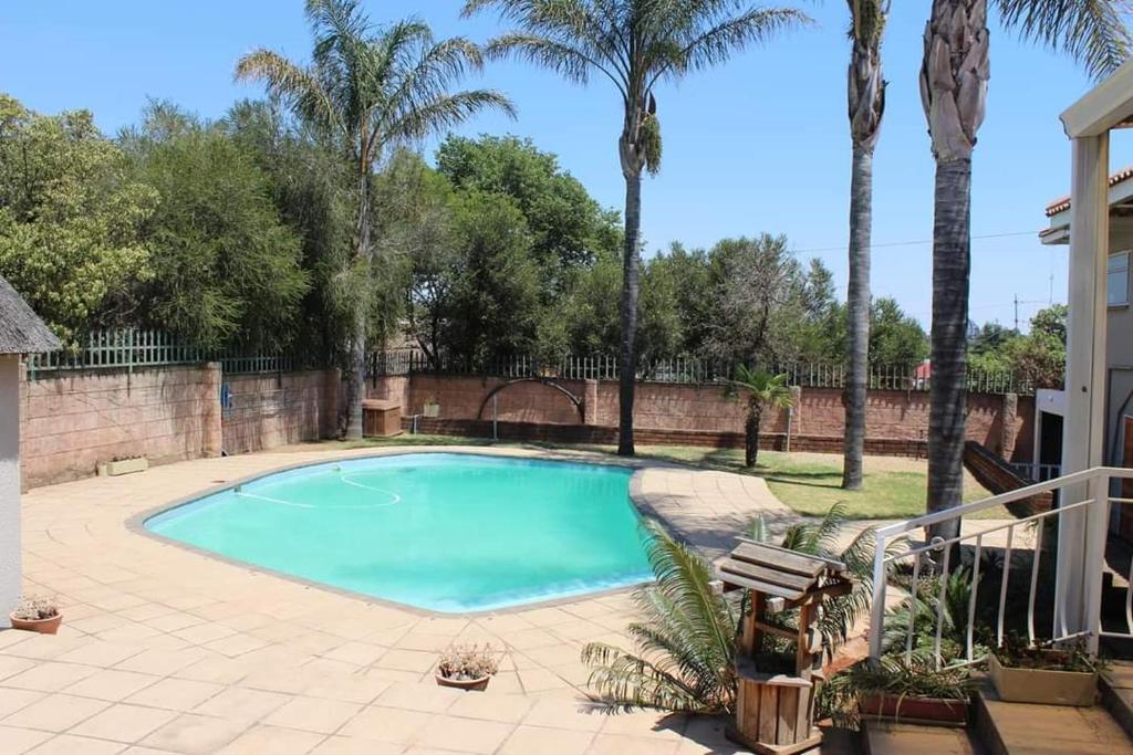 a swimming pool in a yard with palm trees at Swartbessie Geusthouse in Krugersdorp