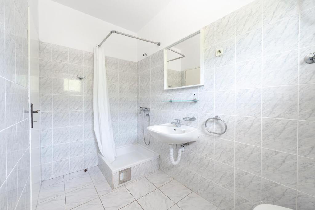 a white bathroom with a sink and a shower at Apartmani Ivušić in Dubrava
