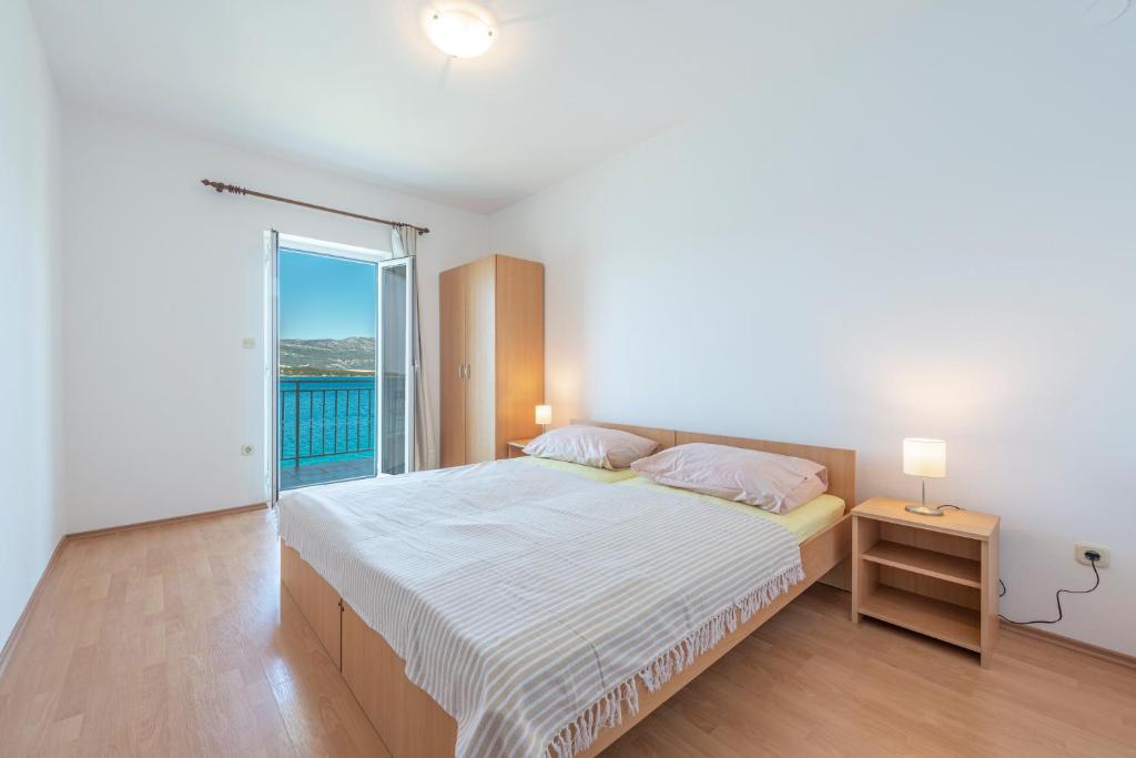 a white bedroom with a bed and a balcony at Apartmani Ivušić in Dubrava