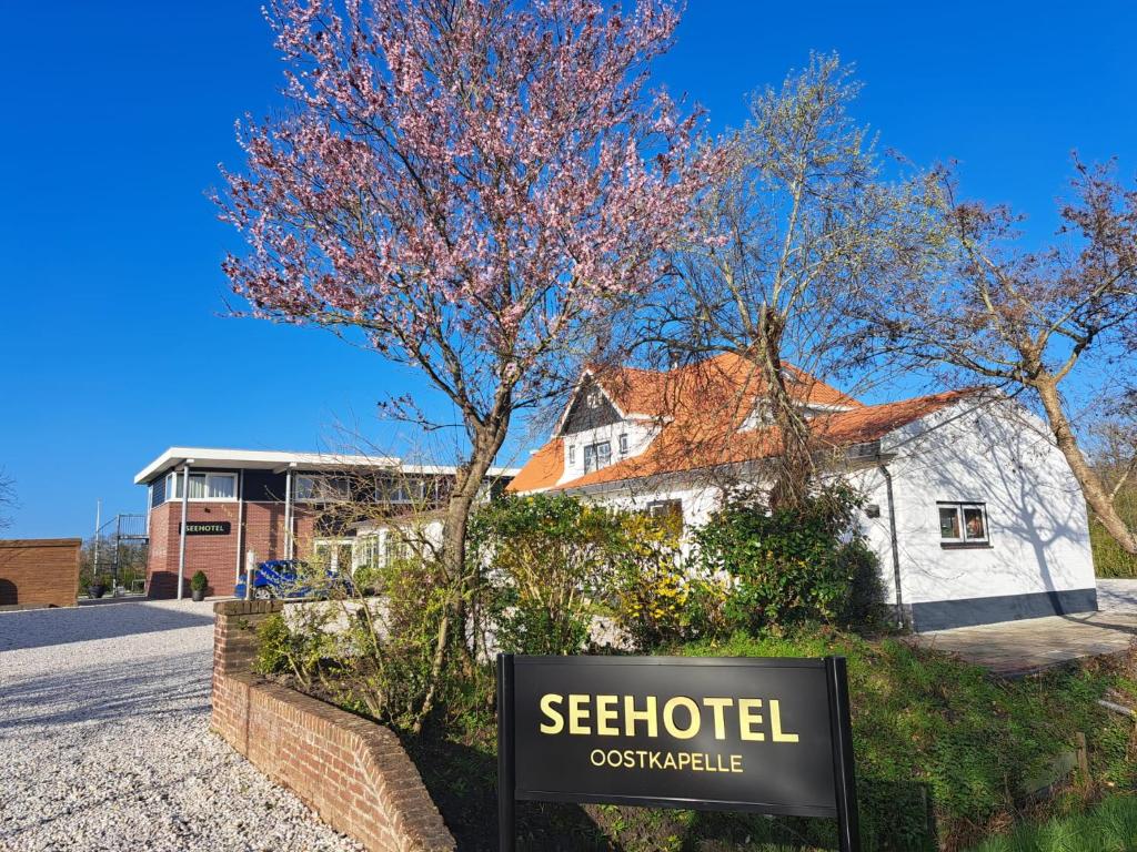 a sign in front of a house with a tree at Seehotel Oostkapelle in Oostkapelle