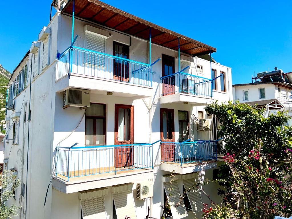 un edificio de apartamentos blanco con balcones azules y árboles en Salina Pansiyon, en Kas