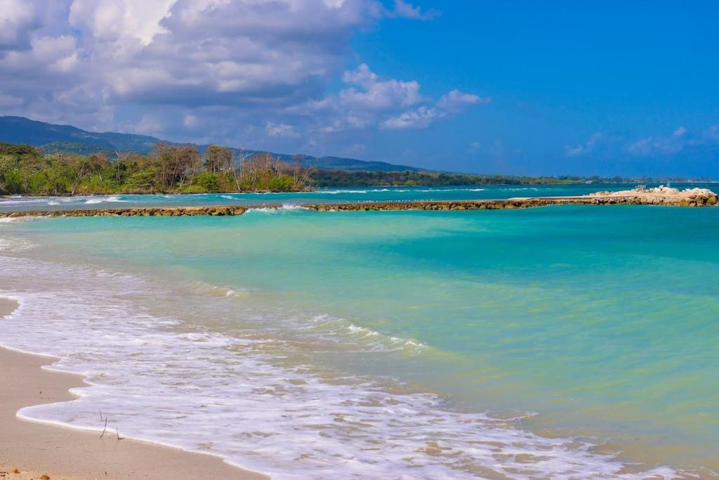 a beach with turquoise water and trees in the background at Beach Holidays at Marina Villa in Saint Annʼs Bay