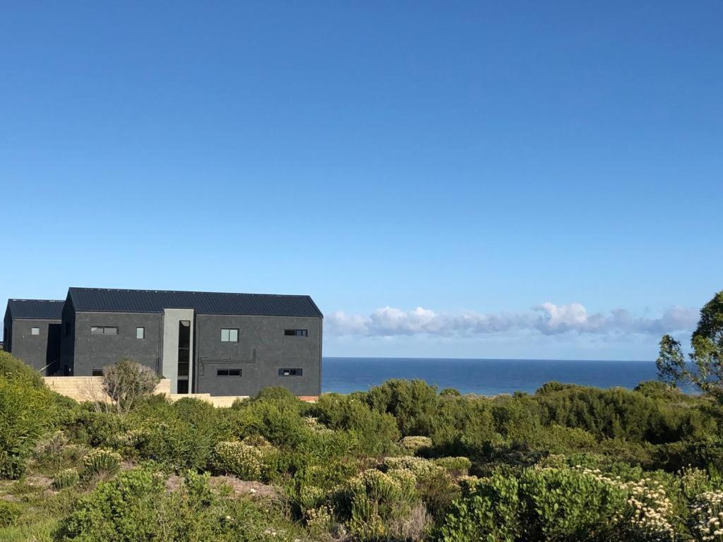 a building on a hill with the ocean in the background at Southern most tip of Africa apartment with sea views in Agulhas