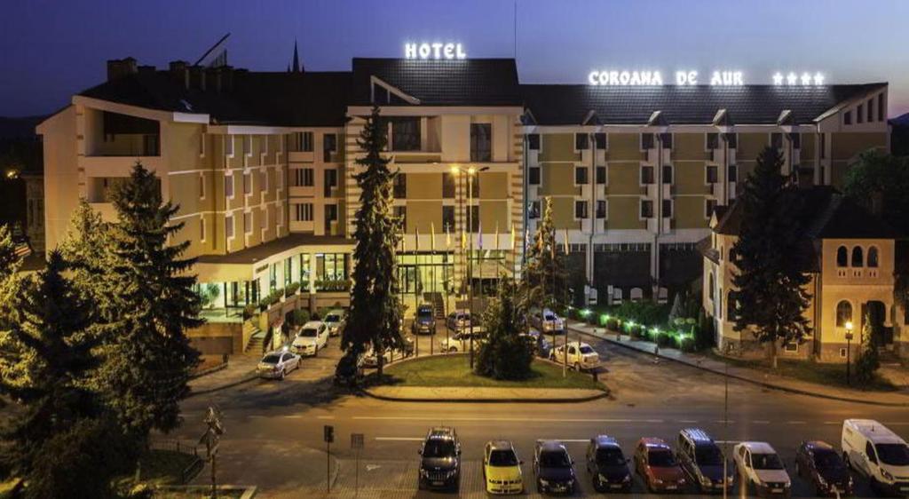 un gran edificio con coches estacionados en un estacionamiento en Grand Hotel Coroana, en Bistriţa