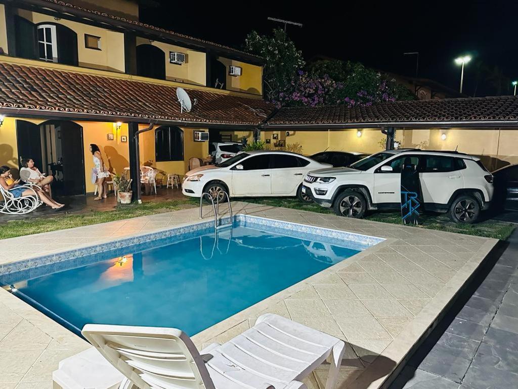a swimming pool with two white chairs and cars parked at ALOHA LAGOON CABO FRIO in Cabo Frio