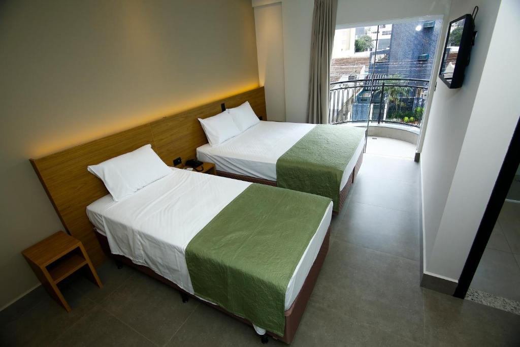 two beds in a hotel room with a balcony at NEO PARK HOTEL in Maringá