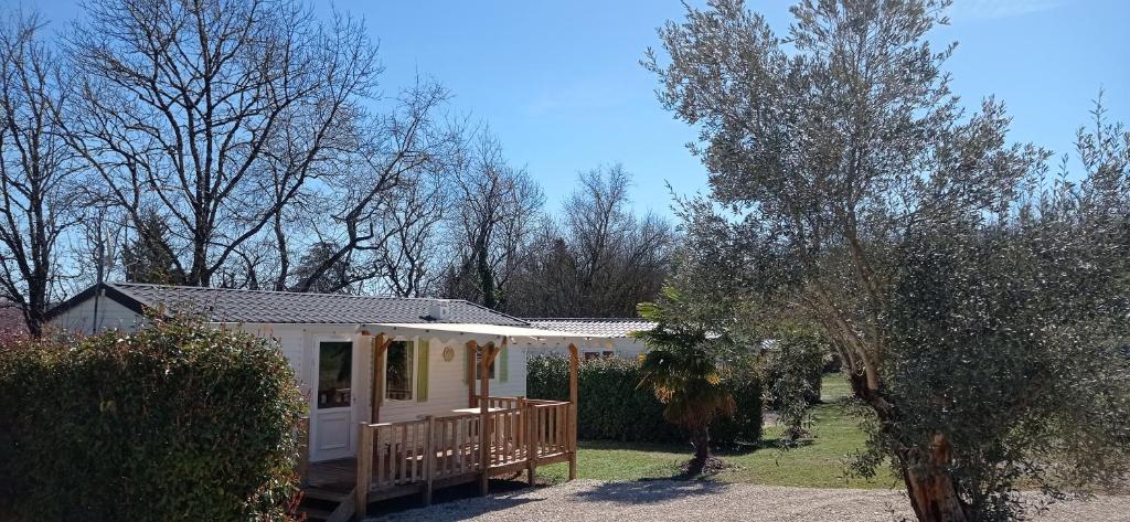 a small white house with a porch and trees at CAMPING LE BEL AIR Mobil home L&#39;OLIVIER 4 personnes in Limogne-en-Quercy