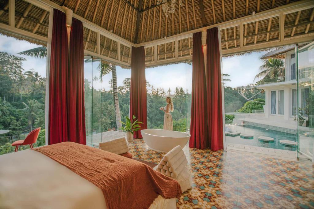 ein Schlafzimmer mit einem Bett und einer Badewanne und eine Frau in einem Fenster in der Unterkunft Villa Cella Bella Ubud in Ubud