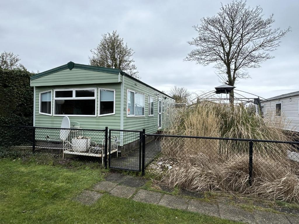 a green tiny house in a yard with a fence at RBR 546 - Beach Resort Kamperland in Kamperland