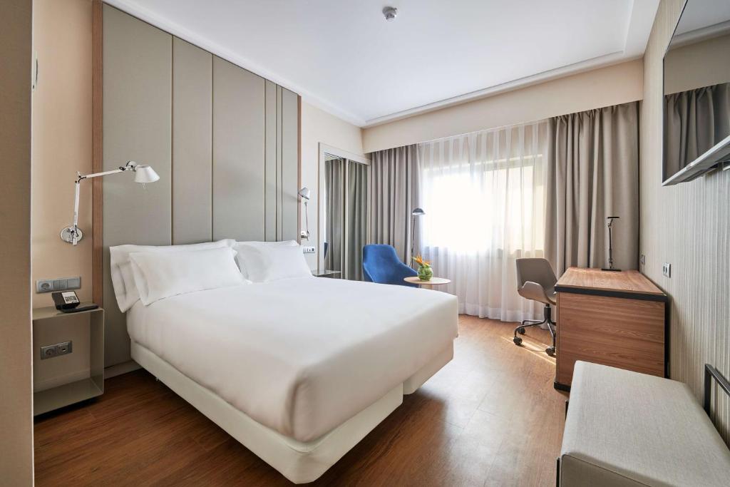 a hotel room with a large white bed and a desk at NH Lisboa Campo Grande in Lisbon