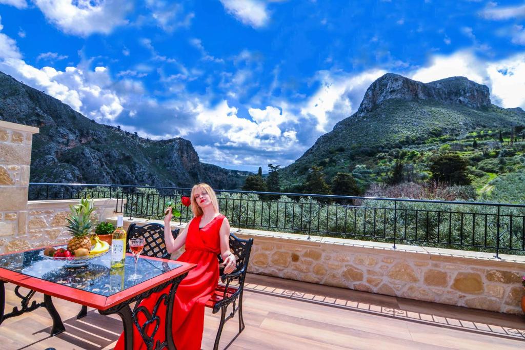 a woman in a red dress sitting at a table on a balcony at Villa Anastasia Luxe with Top WiFi, BBQ & Amazing Views in Kissamos