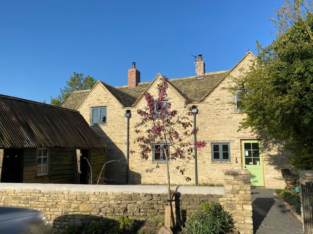 une maison en pierre avec un arbre à fleurs devant elle dans l'établissement High Cogges Farm Holiday Cottages, à Witney