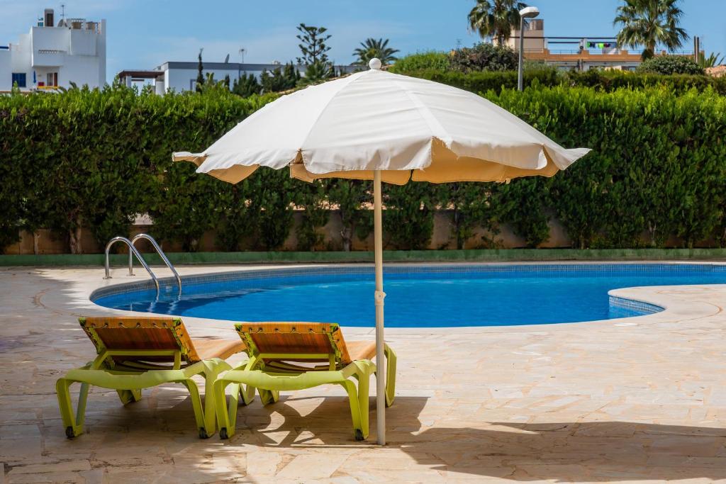 - deux chaises et un parasol à côté de la piscine dans l'établissement Apto con Terraza 104, à Cala Millor