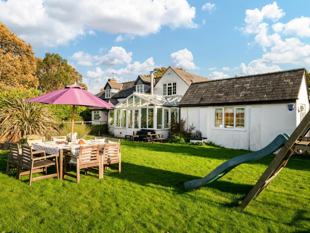 a yard with a table with an umbrella and a slide at Danehurst Cottage in Sway
