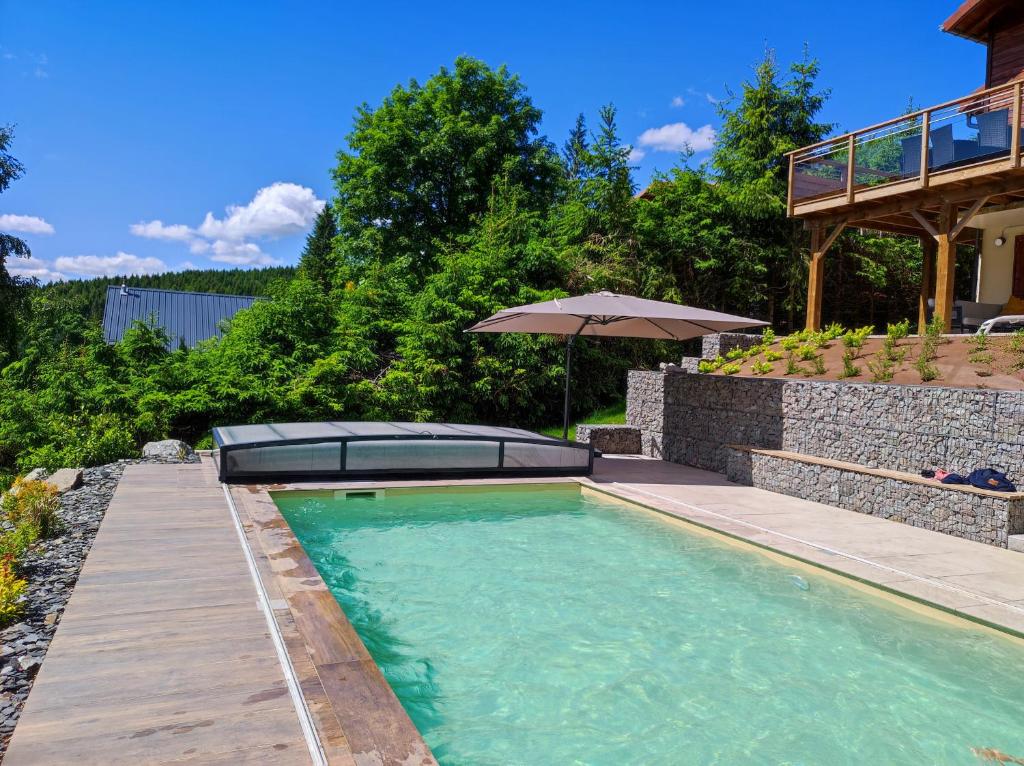 una piscina con una terraza de madera y una sombrilla en Le Cerf, chalet cocooning avec piscine et billard en Ban-sur-Meurthe-Clefcy
