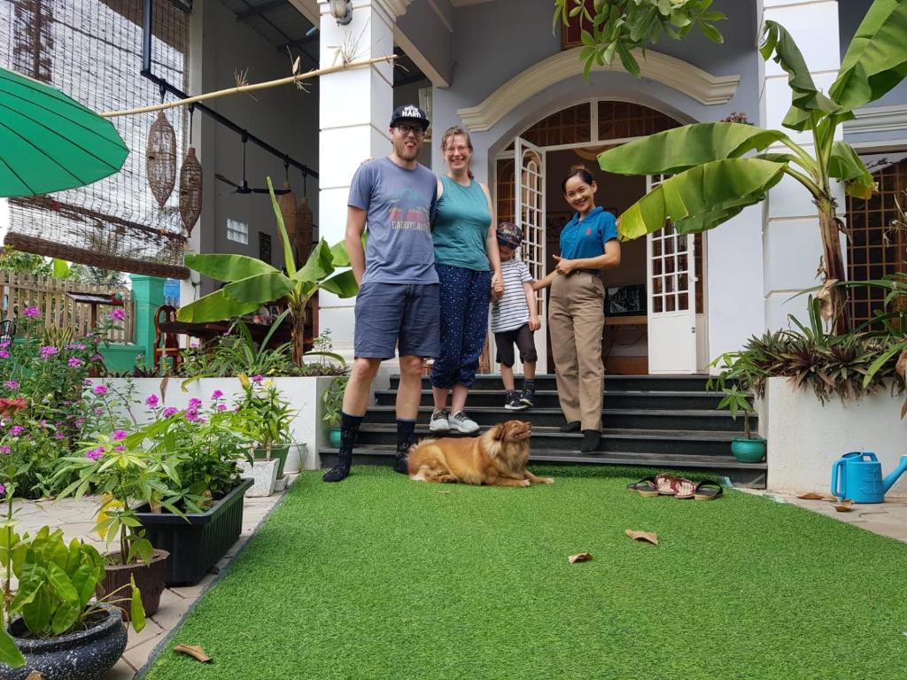 una familia parada frente a una casa con un perro en la hierba en Bloom Garden Bed & Breakfast en Siem Riep