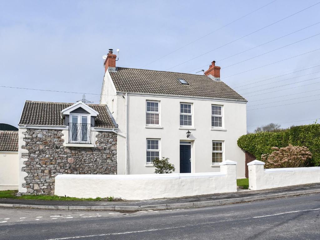 a white house with a stone fence in front of a street at Y Parlwr in Kidwelly