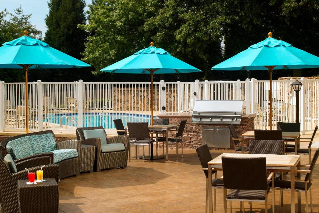 Residence Inn by Marriott Atlanta Cumberland/Galleria في أتلانتا: فناء به طاولات ومظلات زرقاء بجانب مسبح