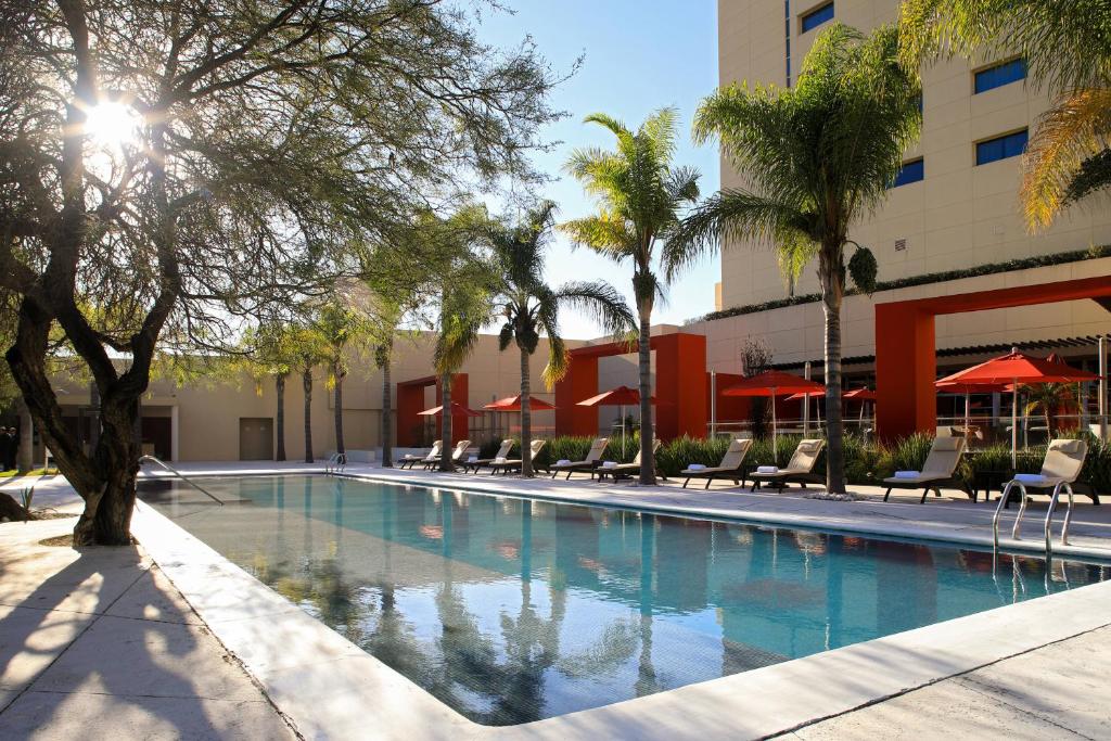 a swimming pool with chairs and trees and a building at Aguascalientes Marriott Hotel in Aguascalientes