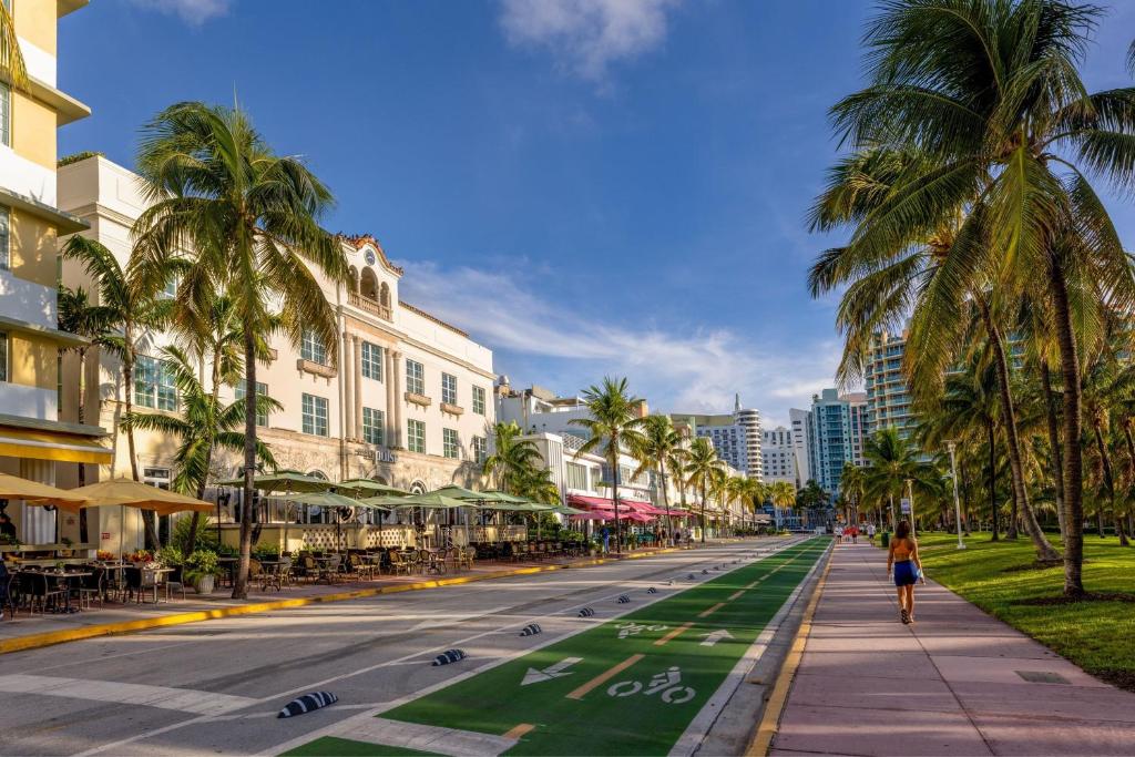 a woman walking down a street with palm trees and buildings at Marriott Vacation Club®, South Beach    in Miami Beach