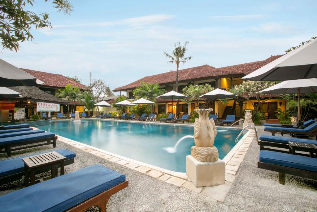 a pool at a resort with blue chairs and a statue at Legian Paradiso Hotel in Legian