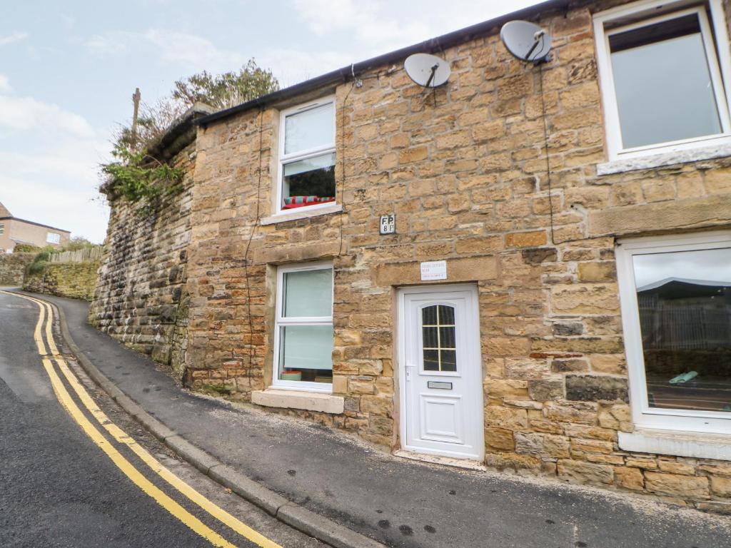 a stone building with a white door on a street at Bridge Cottage in Haltwhistle