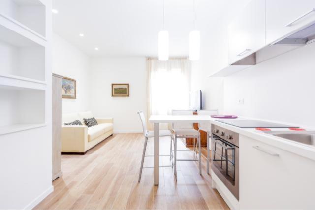 a white kitchen with a table and a living room at Corte Spagnola in Verona