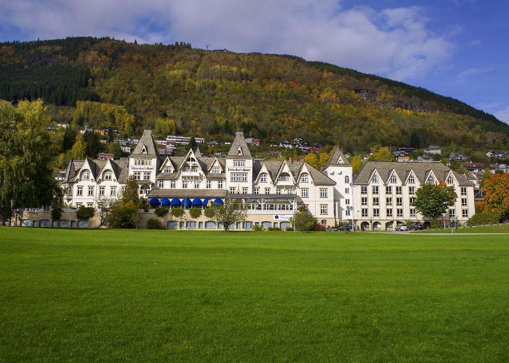 a large building with a green field in front of a mountain at Fleischer's Hotel in Vossevangen