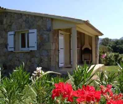 ein Steinhaus mit roten Blumen davor in der Unterkunft Les bergeries d'Ogliastrello in Figari
