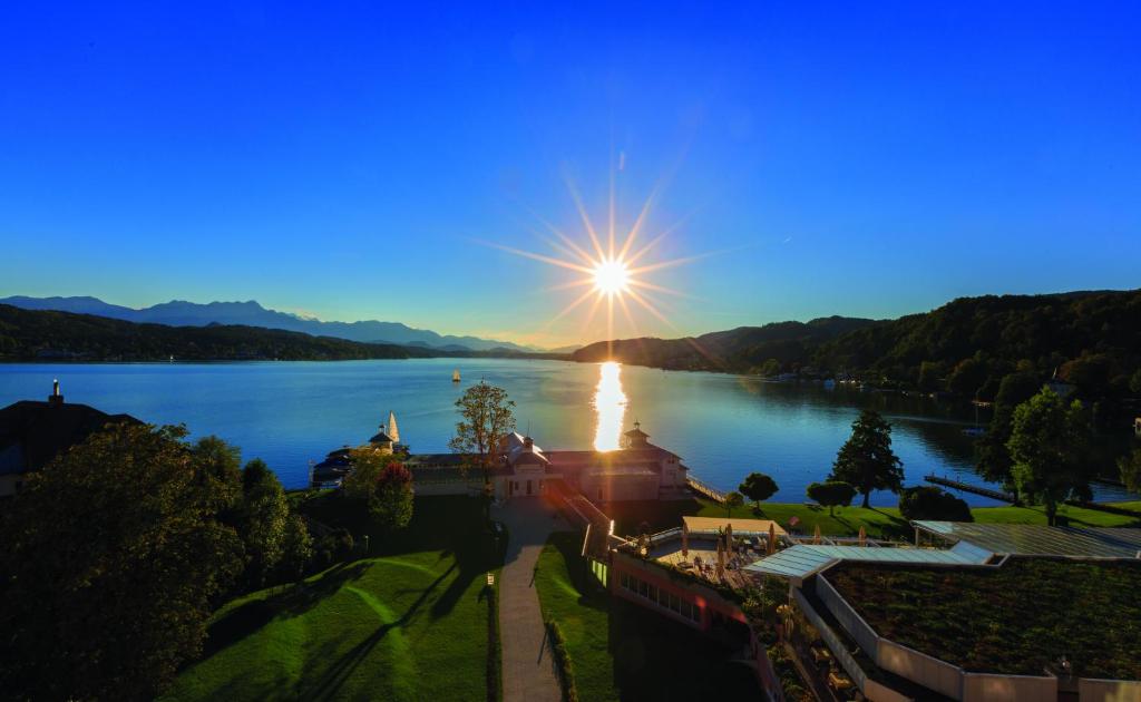 a view of a lake with the sun shining on the water at Werzers Hotel Resort Pörtschach in Pörtschach am Wörthersee
