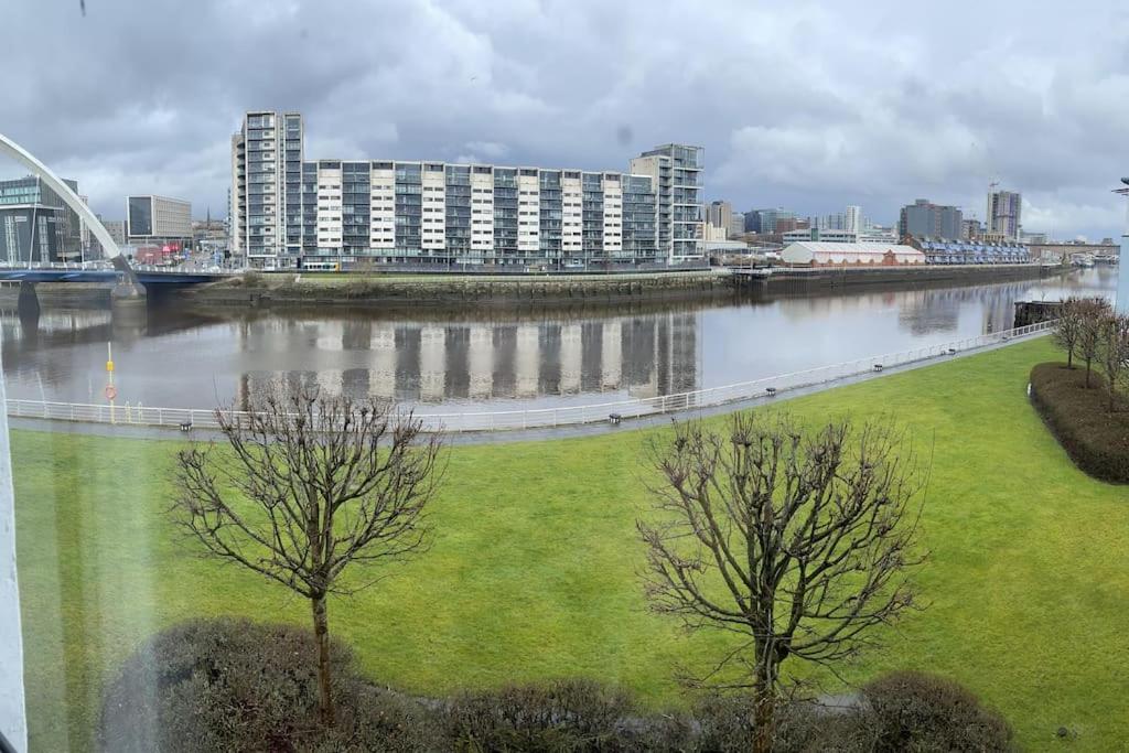 two trees in a field next to a river with buildings at River view Apartment in Glasgow