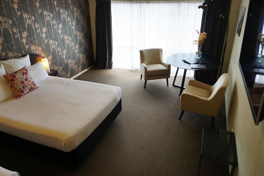 B-Ks Premier Motel Palmerston North في بالمرستون نورث: غرفة فندقية بسرير وطاولة وكراسي