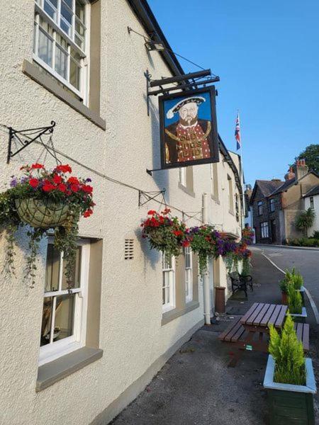 un bâtiment avec des paniers de fleurs et un panneau sur celui-ci dans l'établissement Old Kings Head, à Broughton-in-Furness