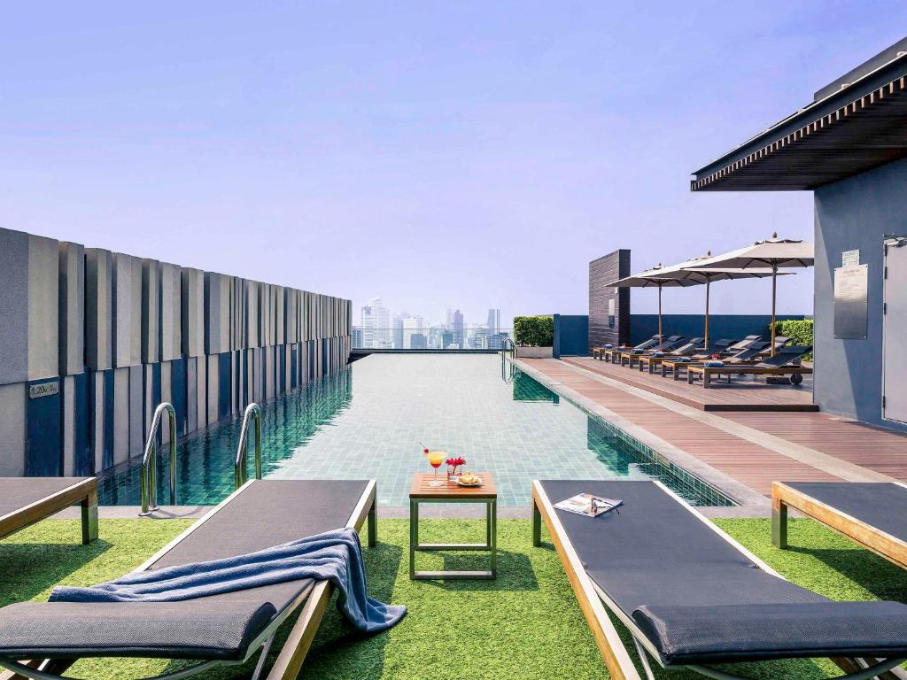a pool on the roof of a building with lounge chairs at Mercure Bangkok Siam in Bangkok
