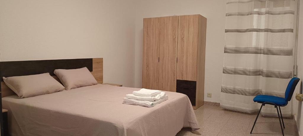 Un dormitorio con una cama con sábanas blancas y una silla azul. en Maravilloso piso de dos dormitorios en Huéscar, en Huéscar