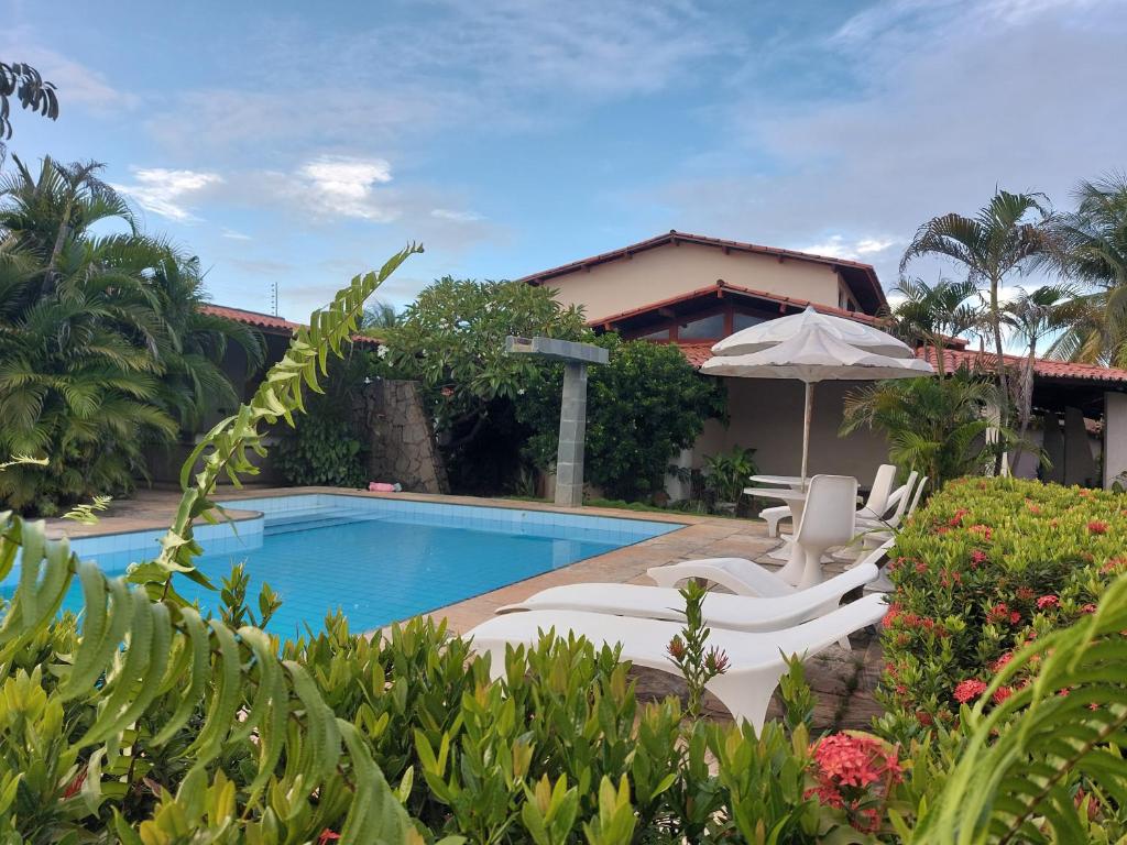 a resort with a swimming pool with chairs and an umbrella at Cumbuco - Casa de praia com piscina e deck in Cumbuco