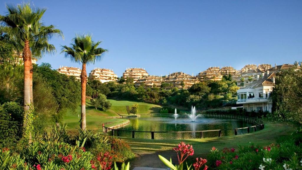 New refurnished Apartment Elviria Hills Marbella في مربلة: حديقة بها نافورة والنخيل والمنازل