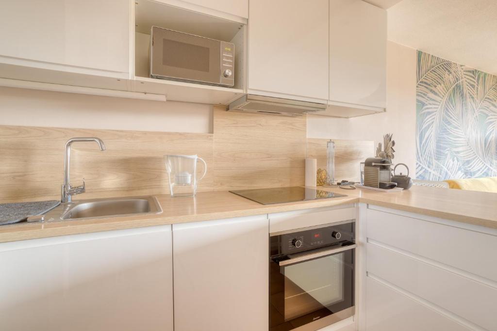 a kitchen with white cabinets and a sink and a microwave at Bel appartement classé 3 étoiles in Bormes-les-Mimosas