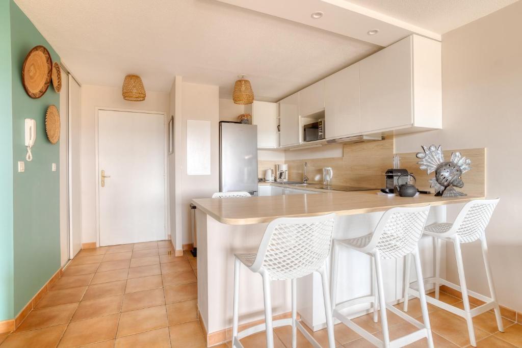 a kitchen with white cabinets and bar stools at Bel appartement classé 3 étoiles in Bormes-les-Mimosas