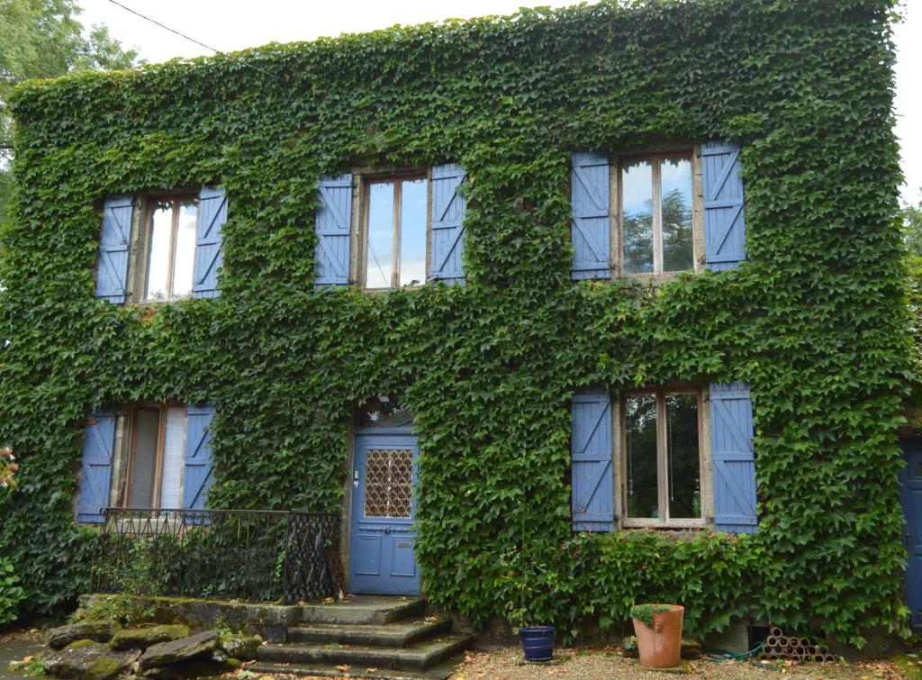 una casa cubierta de hiedra con una puerta azul en Le Puy Robin, en La Souterraine