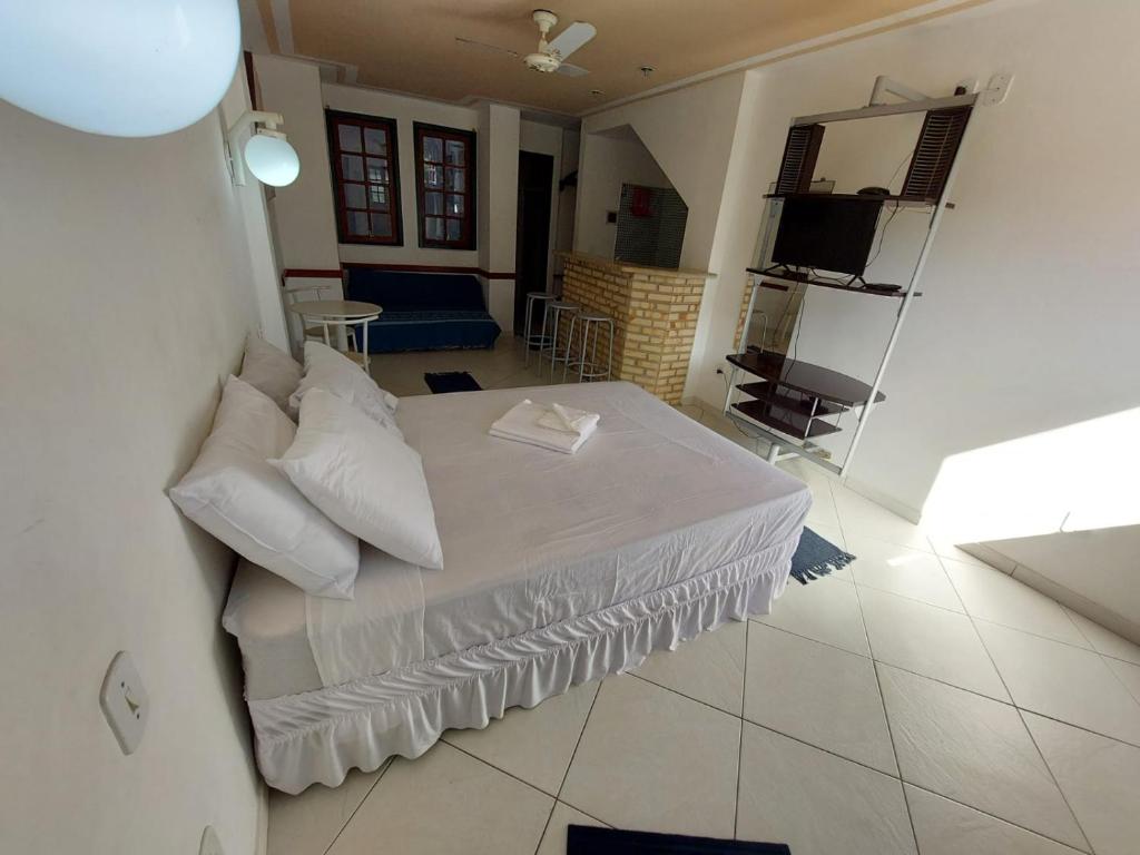 1 dormitorio con 1 cama blanca y TV en Arraial Flats, en Arraial do Cabo