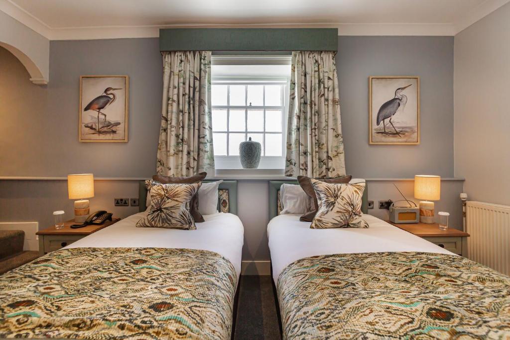 two beds in a hotel room with a window at The Manor Coastal Hotel & Inn, Blakeney - part of The Coaching Inn Group in Blakeney