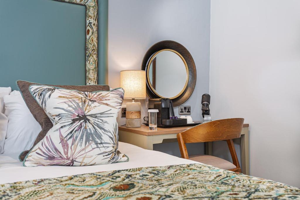 a bed with a pillow and a mirror on a table at The Manor Coastal Hotel & Inn, Blakeney - part of The Coaching Inn Group in Blakeney